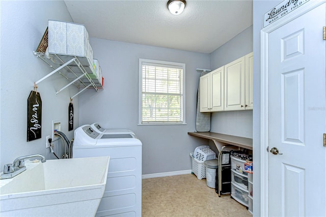 clothes washing area with washer and clothes dryer, baseboards, a textured ceiling, a sink, and cabinet space