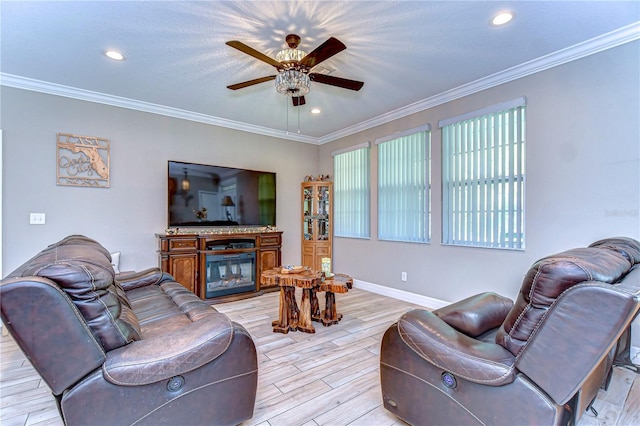 living area with a glass covered fireplace, crown molding, light wood finished floors, and ceiling fan