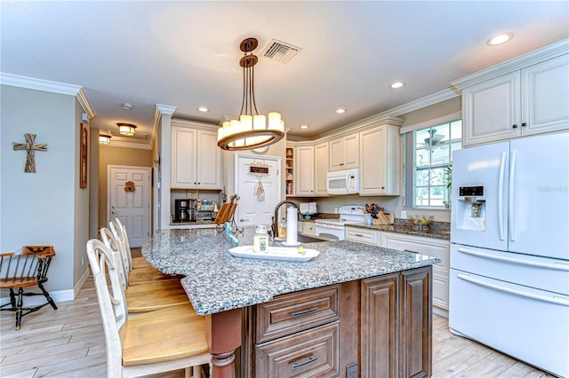 kitchen with light stone counters, a sink, white appliances, visible vents, and ornamental molding