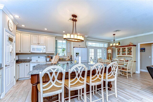 kitchen with crown molding, light wood-type flooring, white appliances, visible vents, and dark stone counters