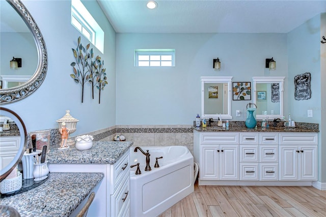 full bath with double vanity, wood finished floors, and a garden tub