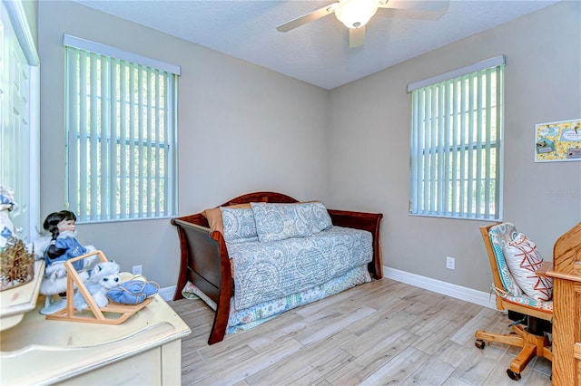 bedroom featuring light wood finished floors, baseboards, ceiling fan, and a textured ceiling