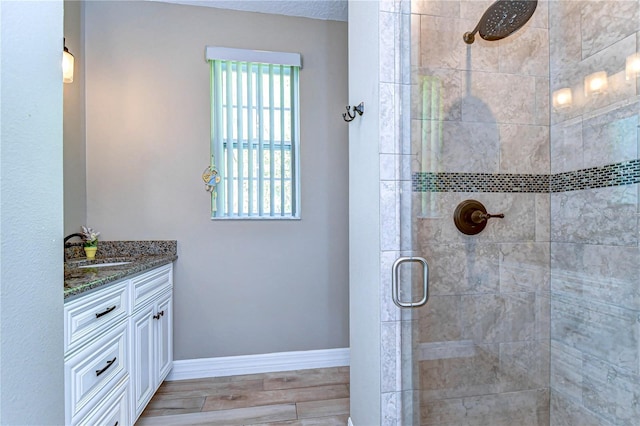 full bath with baseboards, wood finished floors, tiled shower, and vanity