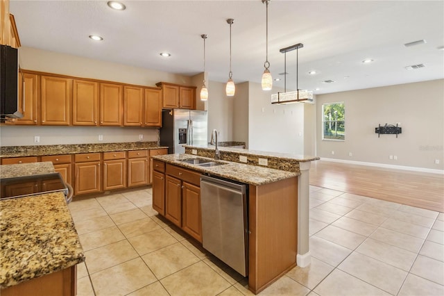 kitchen featuring appliances with stainless steel finishes, a sink, light tile patterned floors, brown cabinetry, and a kitchen island with sink