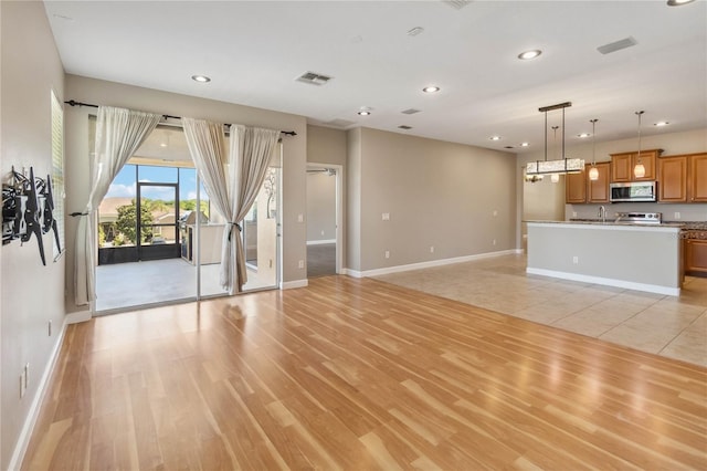 unfurnished living room with baseboards, light wood-type flooring, recessed lighting, and a sink