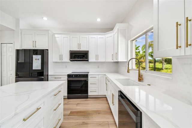 kitchen with tasteful backsplash, white cabinets, a sink, black appliances, and light wood finished floors