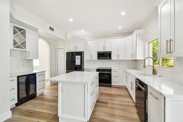 kitchen featuring tasteful backsplash, visible vents, black appliances, a sink, and beverage cooler
