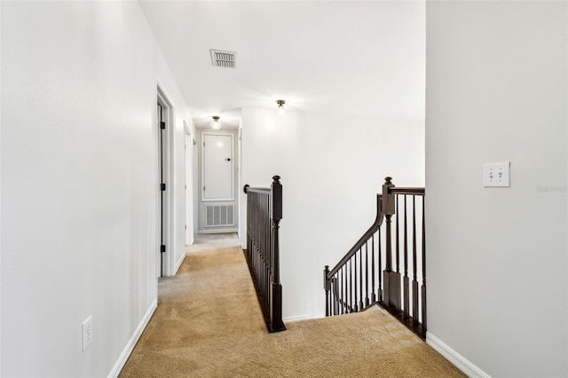 hallway featuring light colored carpet, visible vents, baseboards, and an upstairs landing