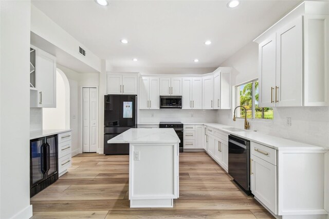 kitchen with visible vents, black appliances, a kitchen island, a sink, and beverage cooler