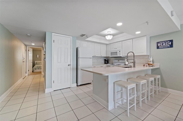kitchen with backsplash, a raised ceiling, a sink, a peninsula, and white appliances