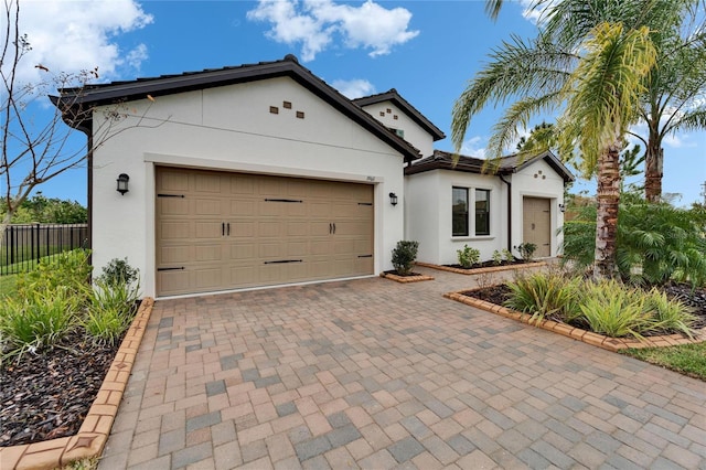 view of front of property featuring stucco siding, decorative driveway, a garage, and fence