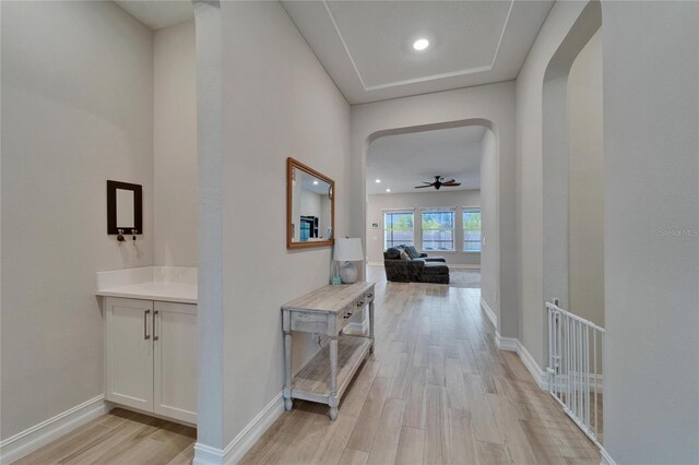 hallway with arched walkways, recessed lighting, baseboards, and light wood-style floors