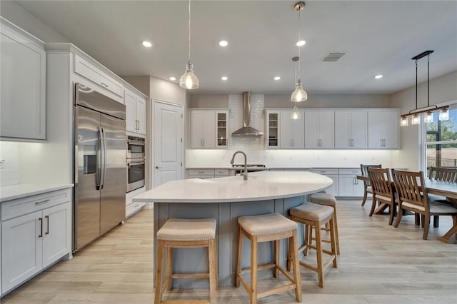 kitchen featuring visible vents, stainless steel appliances, light wood-type flooring, and wall chimney range hood