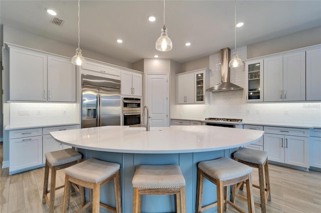 kitchen with a breakfast bar, appliances with stainless steel finishes, light wood-style floors, wall chimney exhaust hood, and a sink