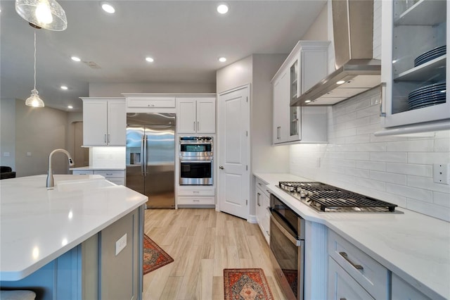 kitchen featuring light wood finished floors, wall chimney range hood, recessed lighting, appliances with stainless steel finishes, and a sink
