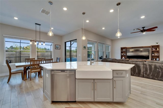 kitchen featuring visible vents, an island with sink, a sink, stainless steel dishwasher, and light countertops