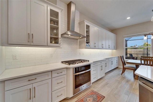 kitchen featuring light countertops, wall chimney range hood, light wood-type flooring, and appliances with stainless steel finishes