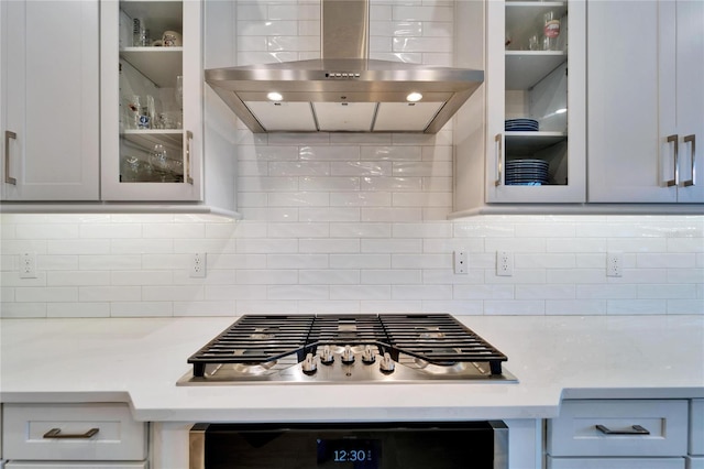 kitchen with backsplash, ventilation hood, light countertops, glass insert cabinets, and stainless steel gas cooktop