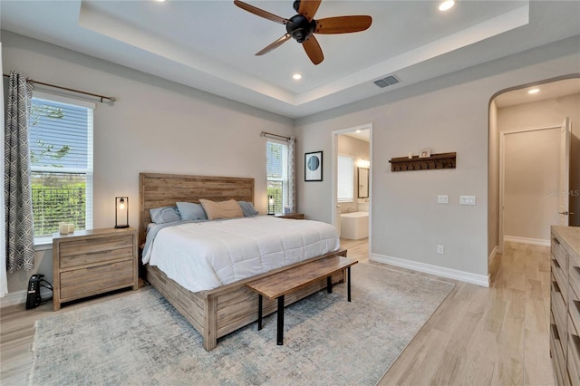bedroom featuring light wood-type flooring, a tray ceiling, and baseboards
