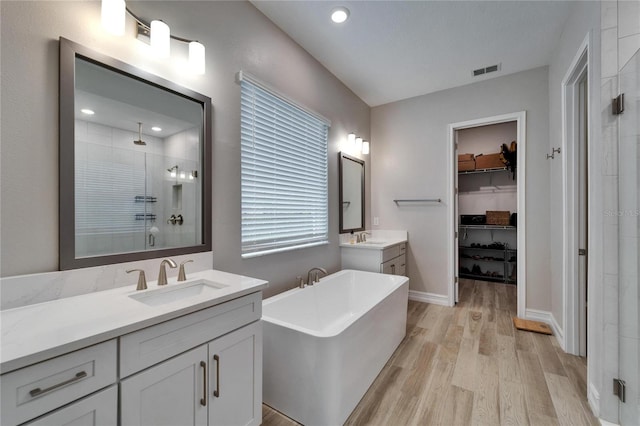full bath with visible vents, a stall shower, a sink, wood finished floors, and a soaking tub