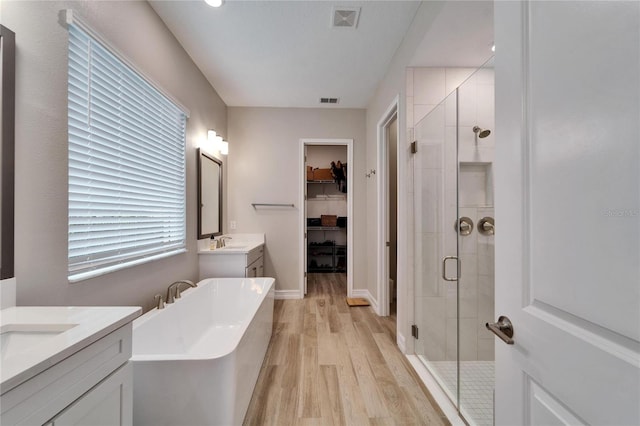 full bathroom featuring visible vents, a stall shower, a sink, wood finished floors, and a freestanding bath