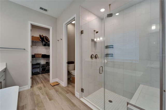 bathroom with visible vents, toilet, a stall shower, wood finished floors, and baseboards