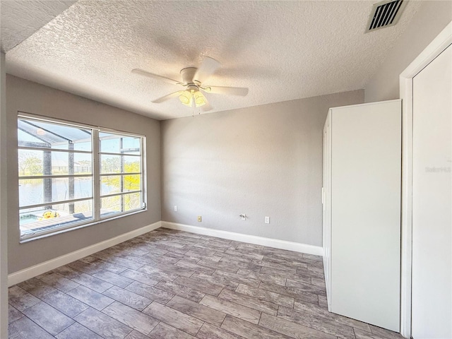 spare room with wood tiled floor, a ceiling fan, a textured ceiling, and visible vents