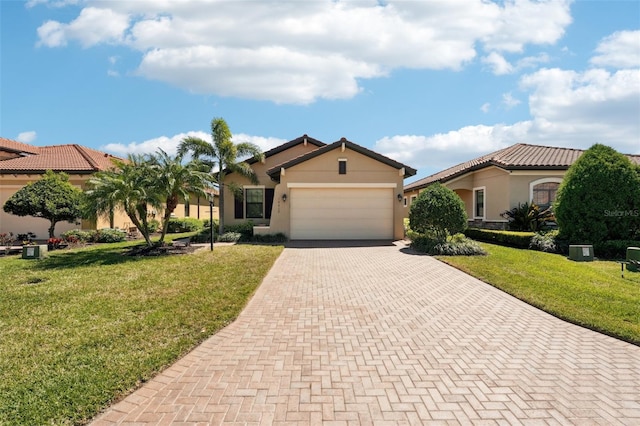 mediterranean / spanish-style home featuring a tile roof, stucco siding, an attached garage, a front lawn, and decorative driveway