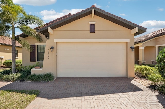 single story home featuring a tiled roof, a garage, decorative driveway, and stucco siding