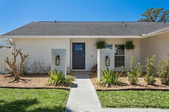 view of exterior entry featuring brick siding and roof with shingles