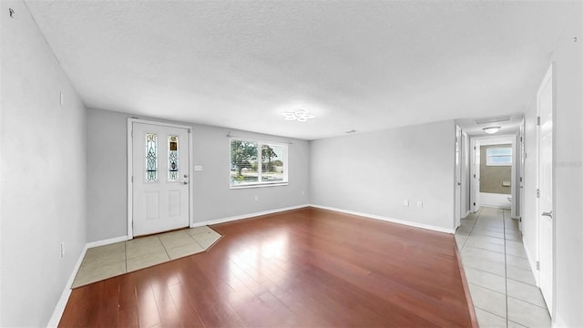 entryway with a textured ceiling, light wood-type flooring, and baseboards