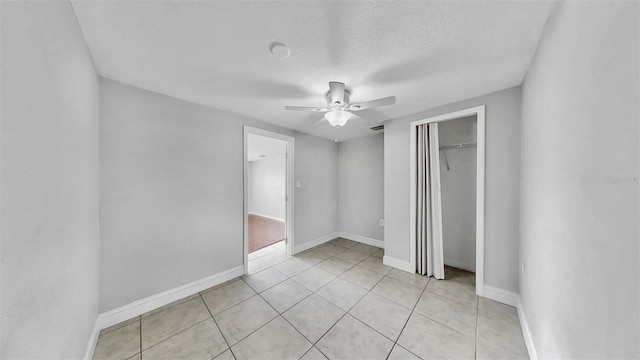 unfurnished bedroom featuring a textured ceiling, a closet, light tile patterned flooring, baseboards, and ceiling fan