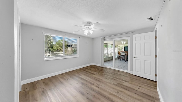 empty room featuring visible vents, a textured ceiling, wood finished floors, baseboards, and ceiling fan