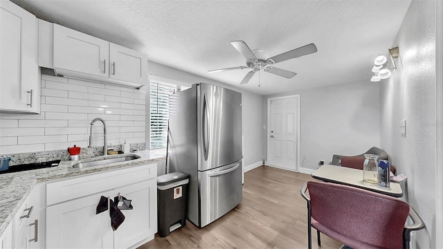 kitchen featuring a ceiling fan, a sink, backsplash, freestanding refrigerator, and light wood-style floors