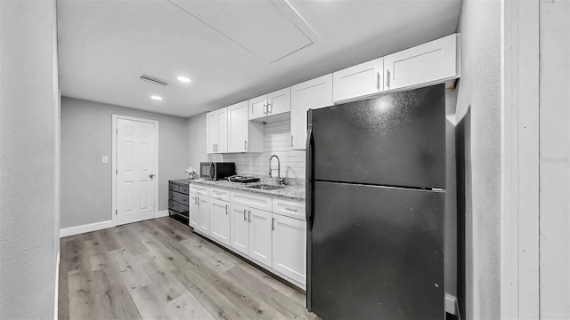 kitchen with light wood-type flooring, visible vents, a sink, stainless steel microwave, and freestanding refrigerator