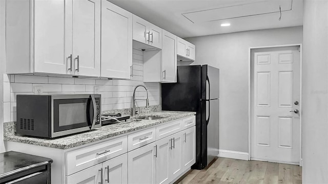 kitchen with tasteful backsplash, stainless steel microwave, light wood-style flooring, white cabinetry, and a sink