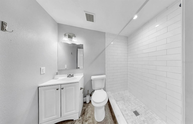 full bathroom with visible vents, toilet, vanity, and a tile shower