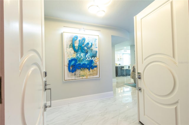 corridor featuring light marble finish flooring and baseboards