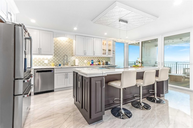 kitchen featuring stainless steel appliances, light countertops, backsplash, a sink, and a kitchen island