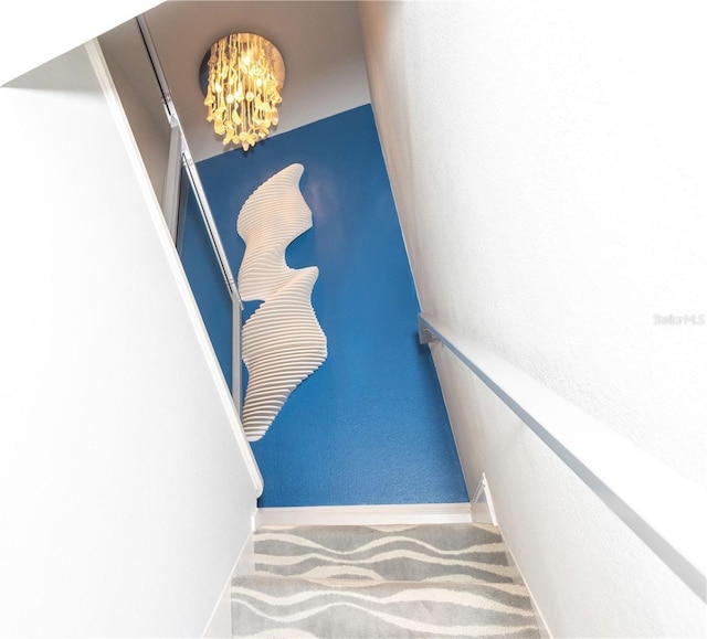 stairs with a chandelier, carpet floors, and baseboards