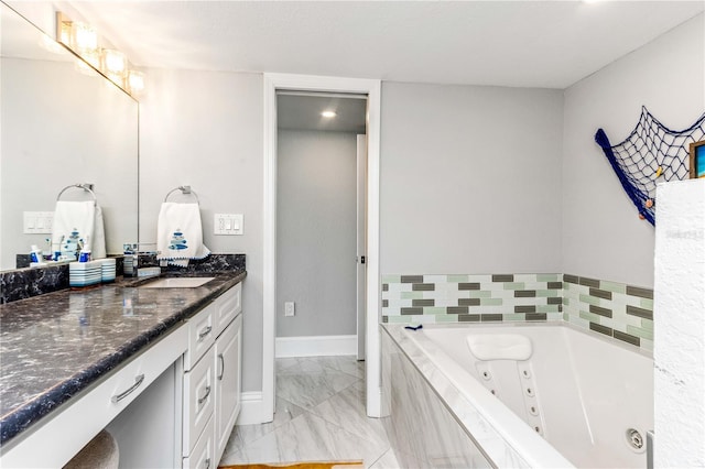 bathroom with marble finish floors, vanity, a jetted tub, and baseboards