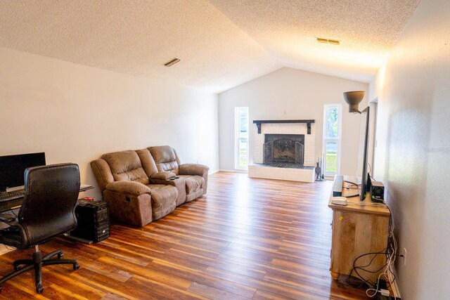 living area with a fireplace, lofted ceiling, wood finished floors, and visible vents