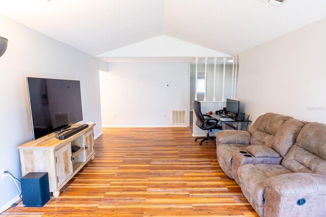 living area featuring visible vents, baseboards, light wood-style floors, and vaulted ceiling