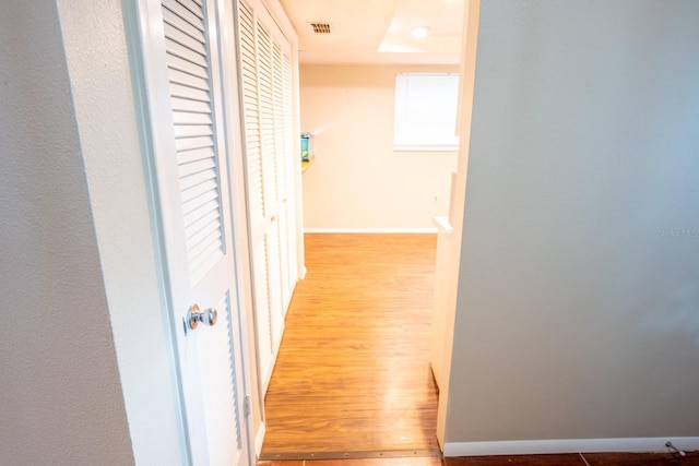 hall featuring visible vents, baseboards, and wood finished floors