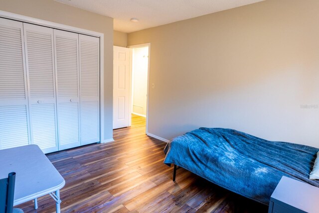 bedroom with wood finished floors, baseboards, and a closet