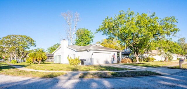 view of front facade featuring stucco siding, a chimney, concrete driveway, a front lawn, and a garage