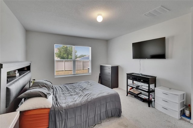 bedroom with a textured ceiling, light colored carpet, and visible vents