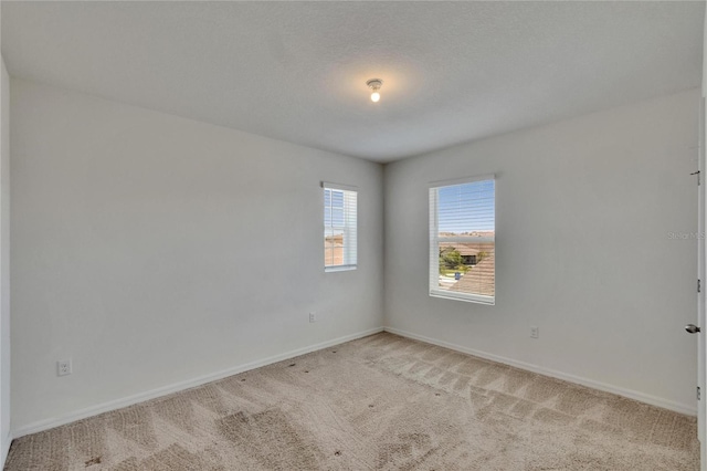 spare room featuring light colored carpet and baseboards