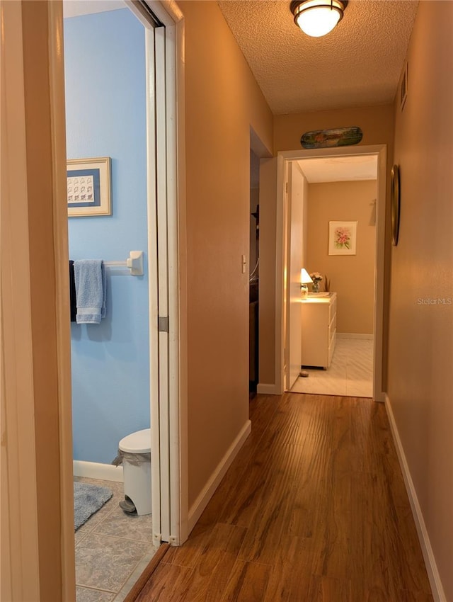 hallway with baseboards, visible vents, a textured ceiling, and wood finished floors