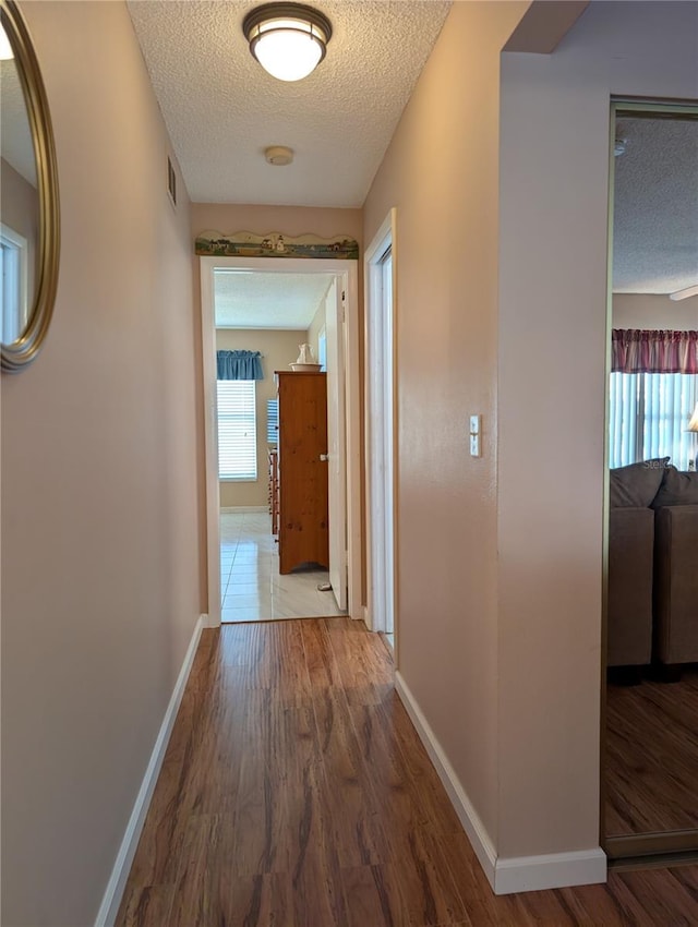 hall featuring a textured ceiling, visible vents, plenty of natural light, baseboards, and wood finished floors